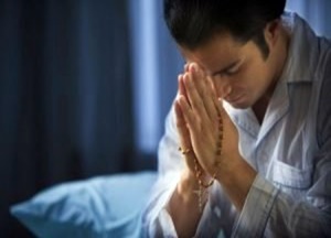 Oração - Homem rezando devotamente com um Terço nas mãos.